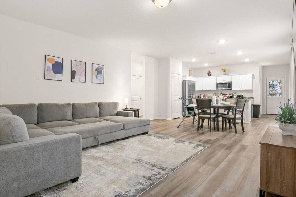 Open-concept living space featuring a spacious sectional, sleek dining area, and a bright kitchen with white cabinetry and stainless steel appliances. Stylish and functional, perfect for modern living and entertaining.