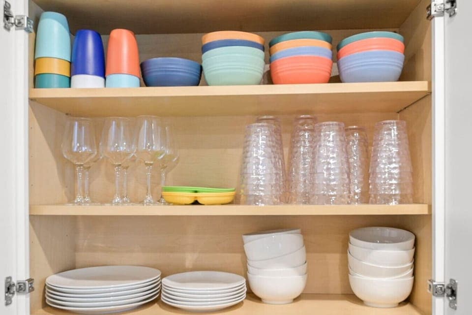 Well-stocked cabinet with colorful mugs, bowls, and kid-friendly dishware alongside sleek glassware and neatly stacked plates. This organized setup offers everything needed for entertaining or casual family meals in style and convenience.