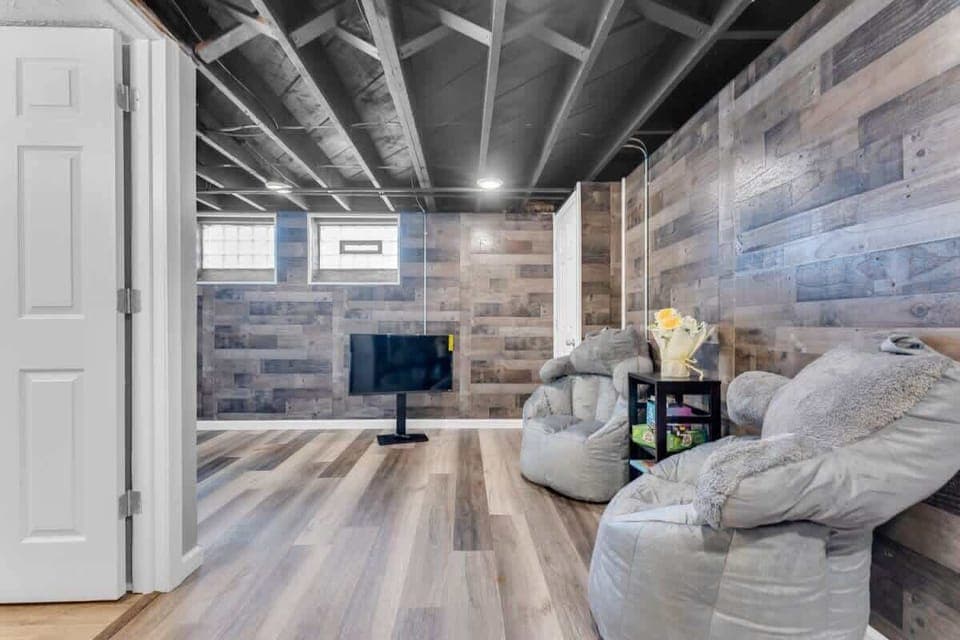 - Basement lounge with wood accent walls and open space   - Beanbag seating for relaxation and casual hangouts   - Mounted TV for entertainment in cozy setting  