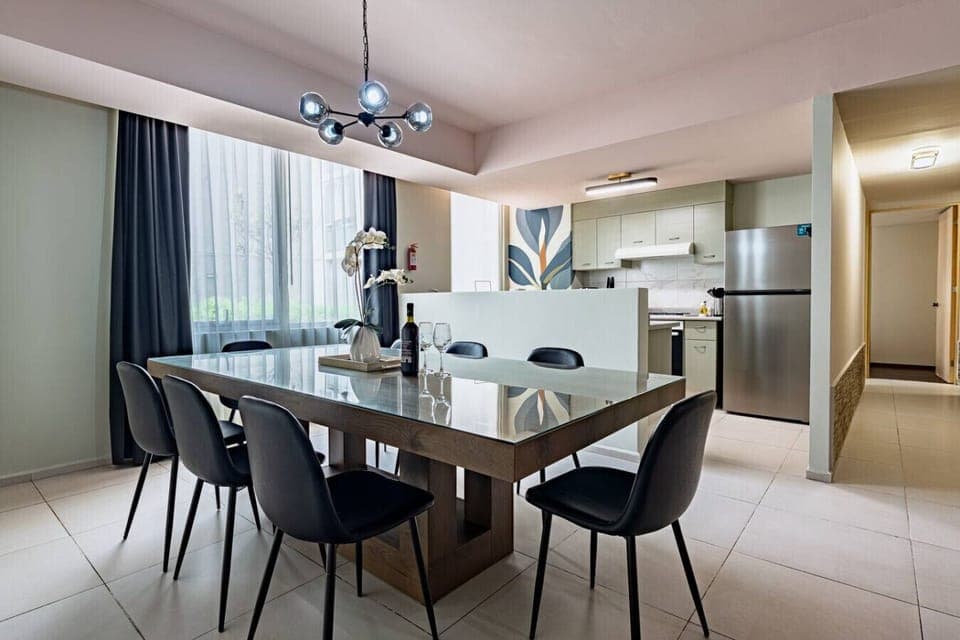 A well-lit dining area with a wooden table, dark chairs, and a view into an adjacent room