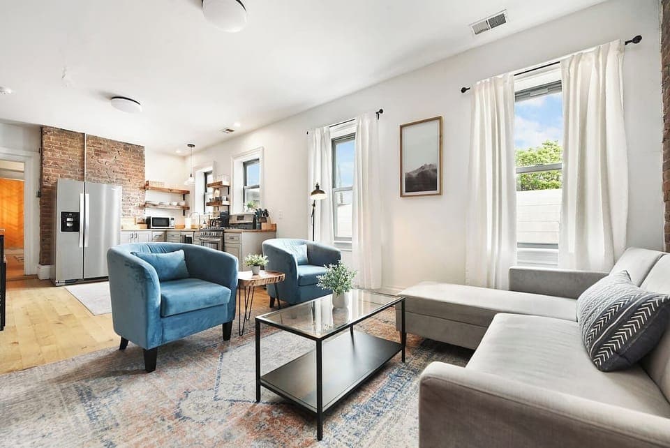 Relax in style on the L-shaped sofa, surrounded by a chic brick wall, floor-to-ceiling windows, and warm lighting. The perfect spot to unwind!