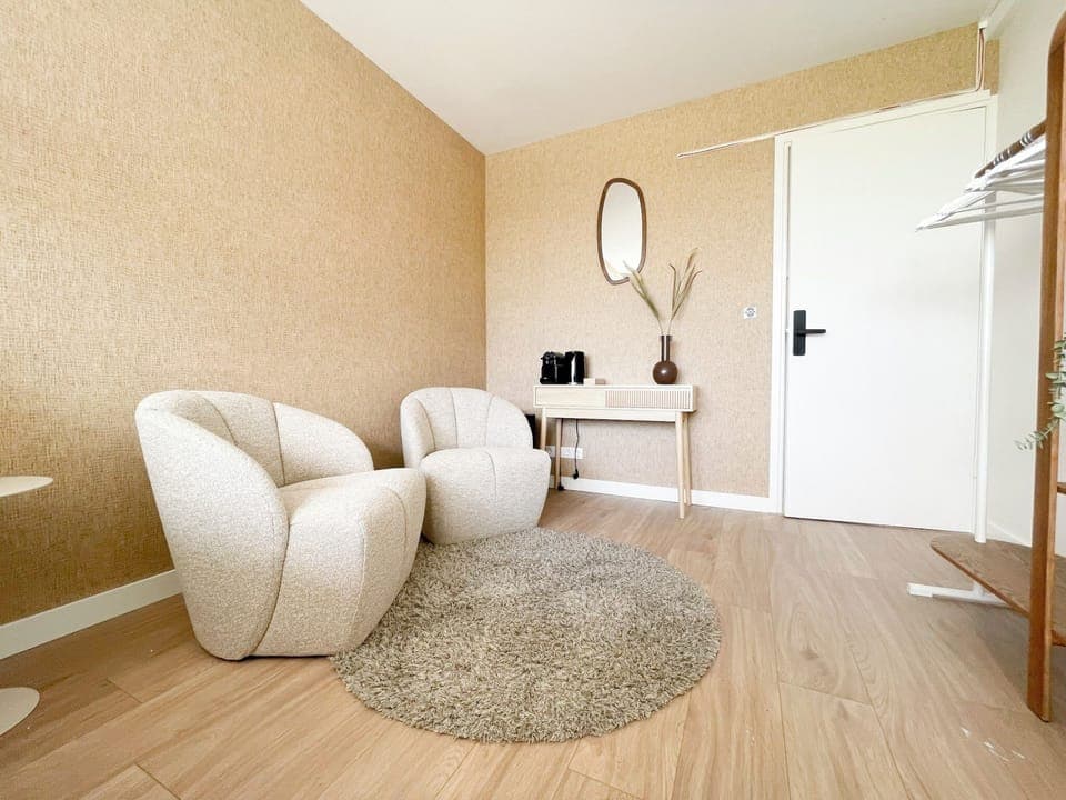 Modern lounge area with soft cream chairs, warm tones, a round rug, and a console with coffee setup and natural decor.