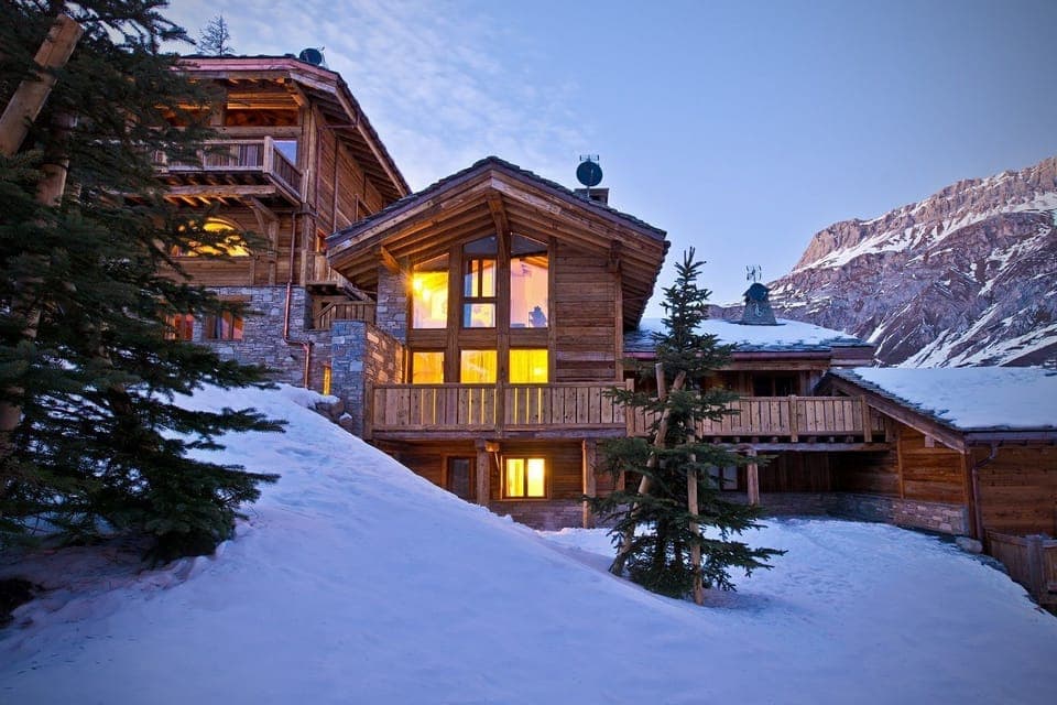 This luxurious chalet exudes rustic charm, showcasing a stunning exterior with warm lighting that complements the surrounding snowy landscape and majestic mountains.