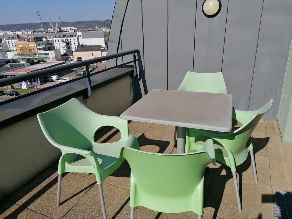 Relax on the charming balcony featuring a modern green furniture set, perfect for sunlit mornings overlooking the cityscape.