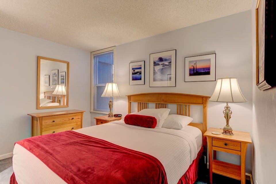 This cozy studio features a queen bed adorned with plush pillows and bedside tables, offering a serene atmosphere enhanced by tasteful artwork.