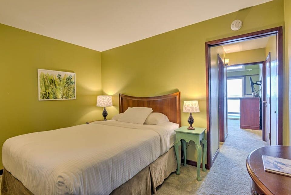 The inviting Queen Bed Mini Suite features a cozy queen bed framed by a warm green wall and ambient lighting.