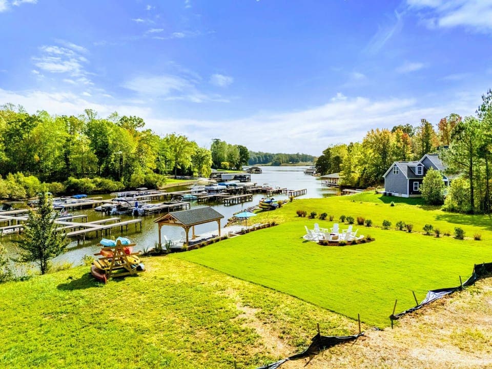 Aerial View - The sprawling lakefront grounds from above, with the dock, pavilion, fire pit circle, playground, and boathouse all in view.
