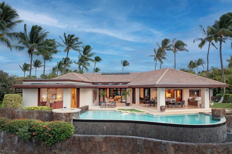 Modern tropical villa with infinity pool surrounded by swaying palms and volcanic stone walls in paradise.