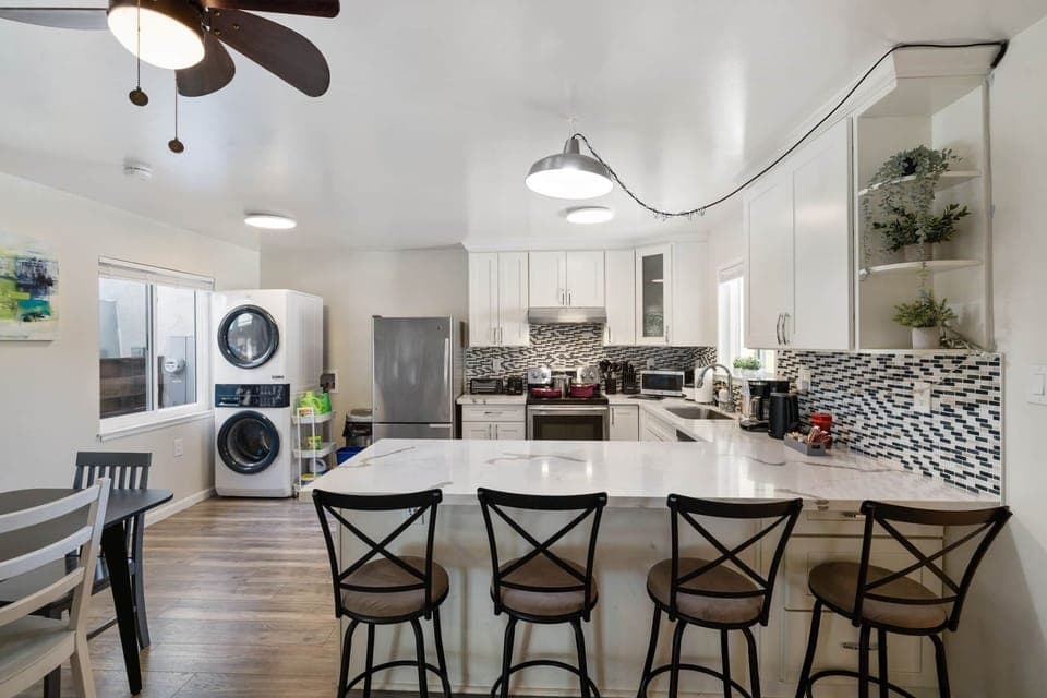 Modern kitchen with island, bar stools, and stacked washer/dryer.