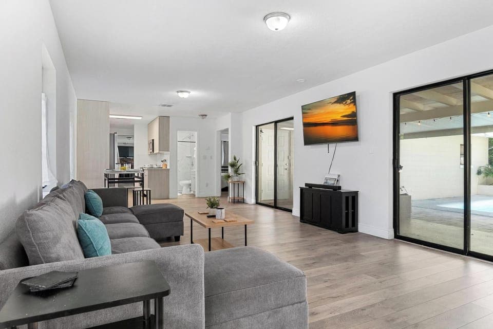 Bright and modern living space with cozy seating, smart TV, and open layout leading to the kitchen and pool area. Perfect for relaxing after a day at the beach or enjoying movie nights with family.