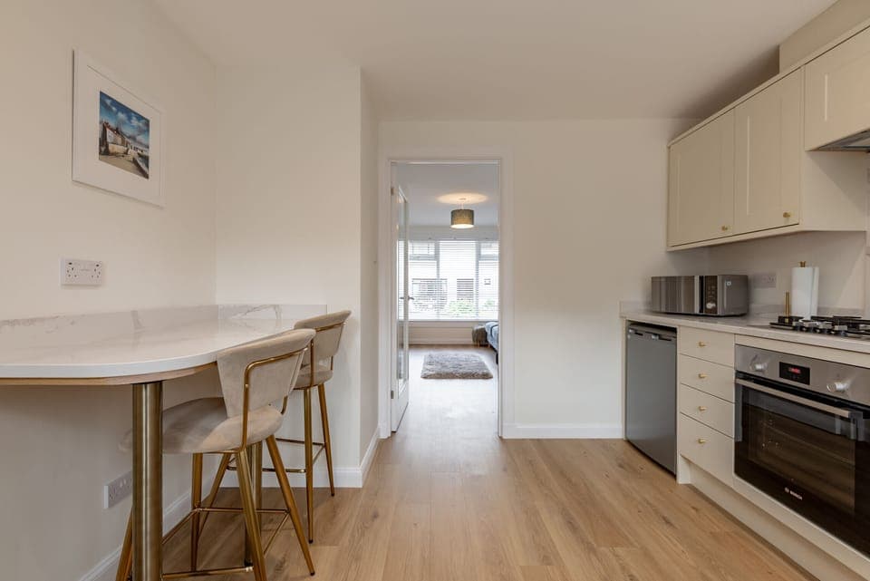 View from modern kitchen featuring cream cabinets and marble breakfast bar into bright living room with large window.