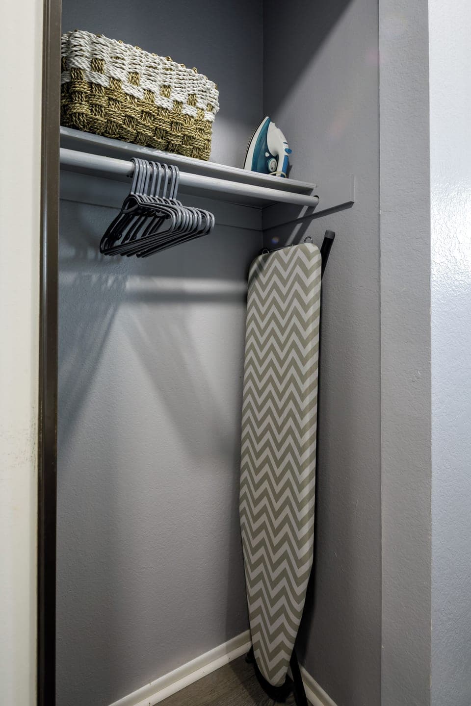 A well-stocked guest closet with hangers, an iron and ironing board, and fresh towels neatly arranged on the top shelf — everything you need for an extended stay.