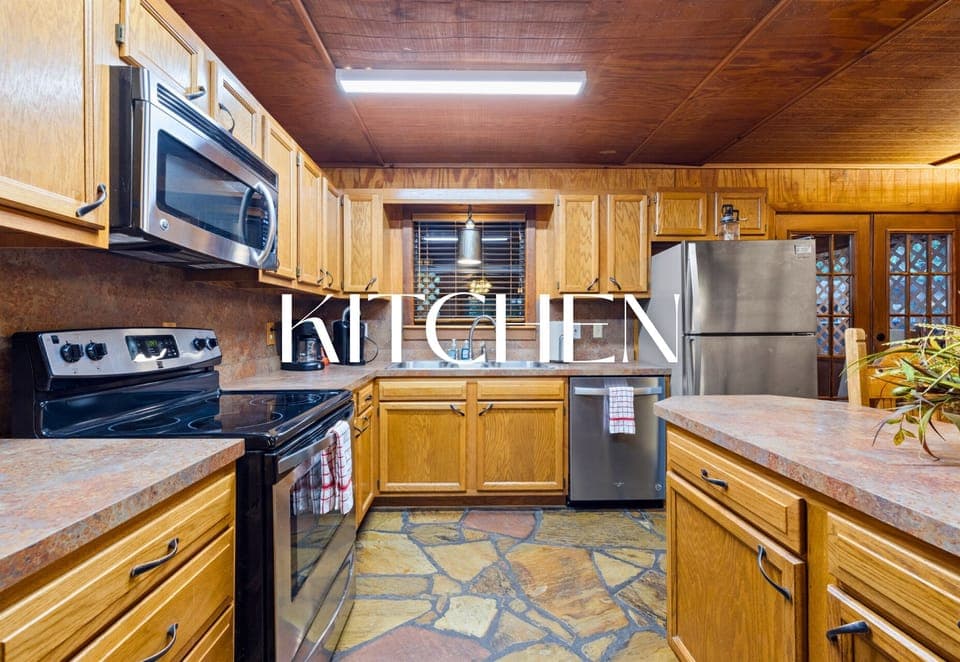 Rustic kitchen with stainless appliances and forest views.