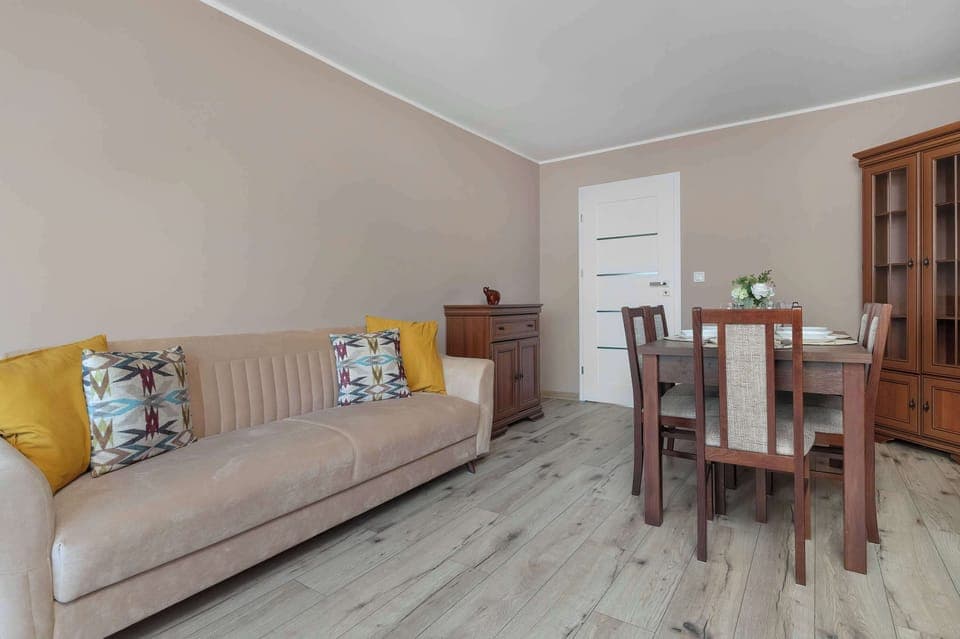 A cozy living room area with a sofa bed and a dining table. Warm tones create an inviting atmosphere.