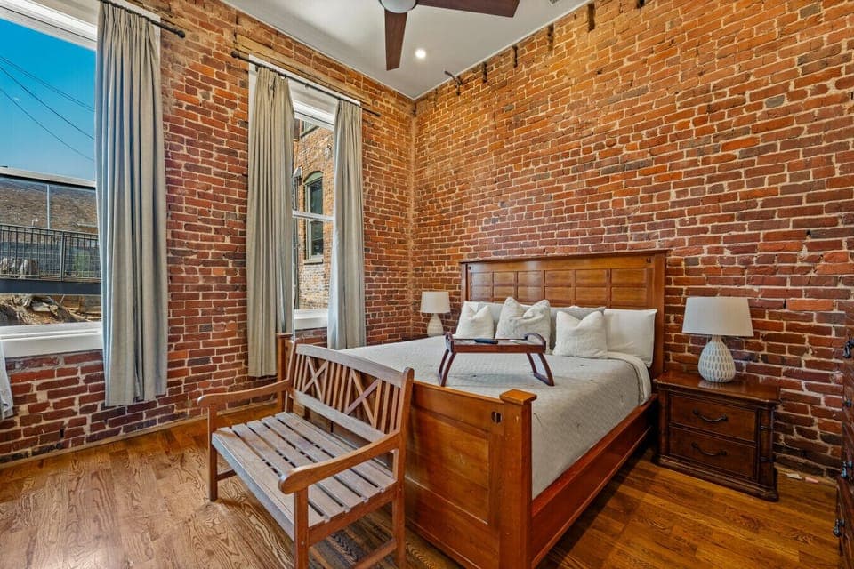 Bedroom 1 | King bed with warm wood furnishings, exposed brick walls, and natural light