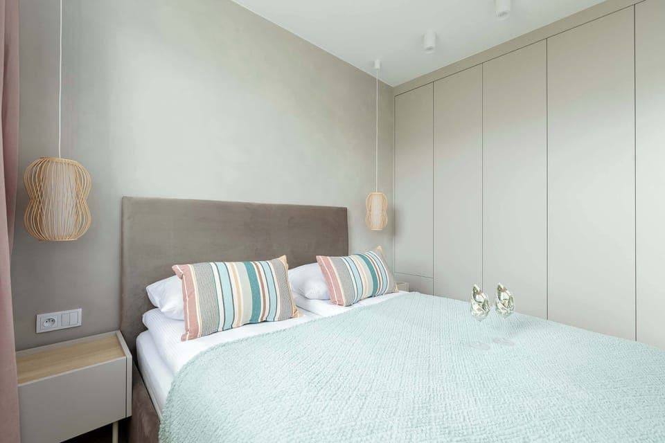 Light-filled bedroom with soft bedding, bedside lamps, and a minimalist wardrobe, offering calm and comfort.