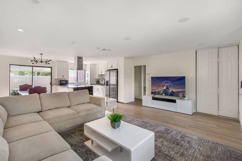 Open-concept living room with high ceilings, comfy seating, gas fireplace, Smart TV, and side yard access.