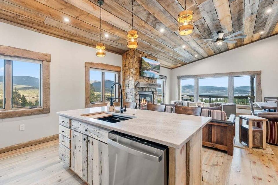 Gather loved ones at 128 GCR 4034 in this stunning open kitchen where rustic wood beams frame breathtaking mountain views through floor-to-ceiling windows.