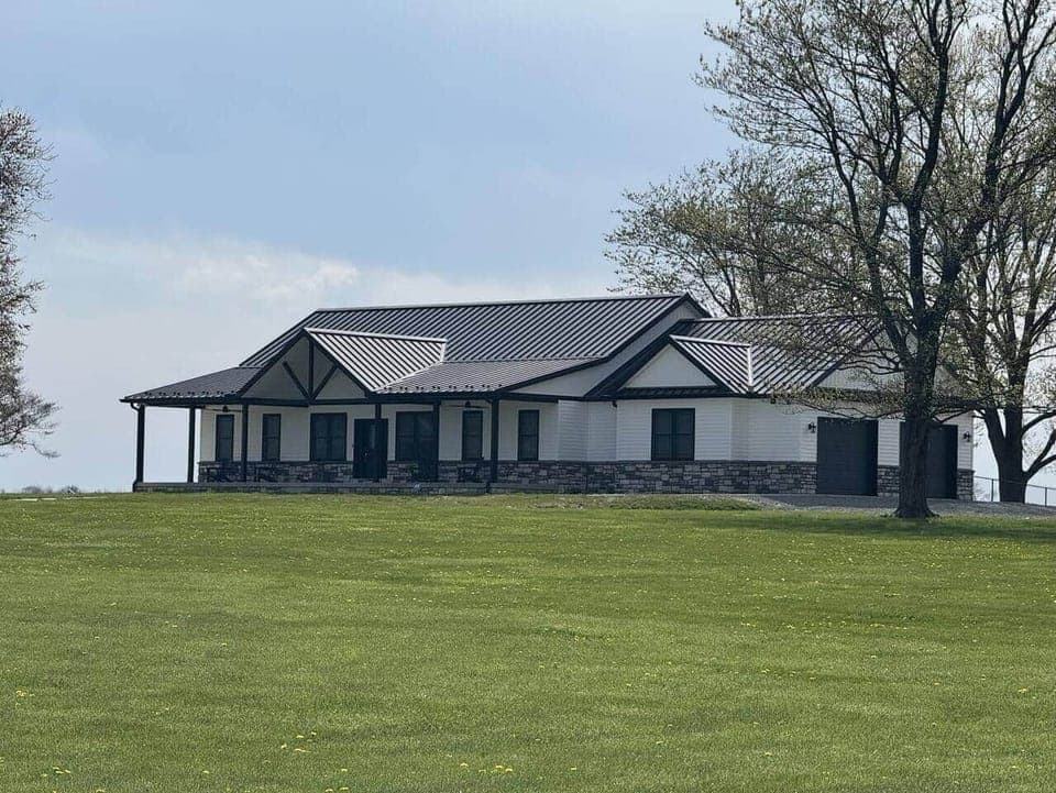 This close-up view highlights the beautiful architectural design and bold contrast of the black metal roof and stone accents. 

The wide porch and symmetrical layout give the home a clean and inviting presence.