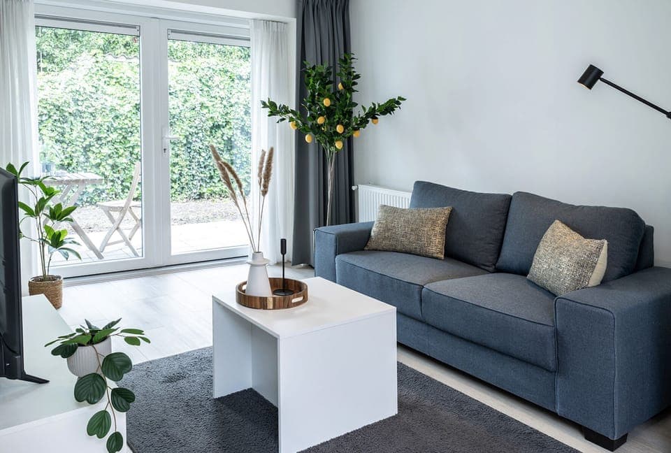 Bright living room with a comfy blue sofa, lemon tree decor, and large garden doors that fill the space with light. Stylish and peaceful atmosphere.