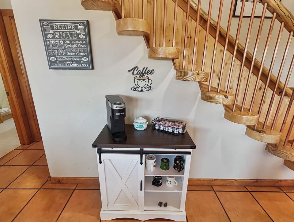 Start your mornings right with this charming coffee station tucked perfectly beneath the rustic wooden staircase. Your personal Keurig awaits to brew that perfect cup while you plan your day's adventures.