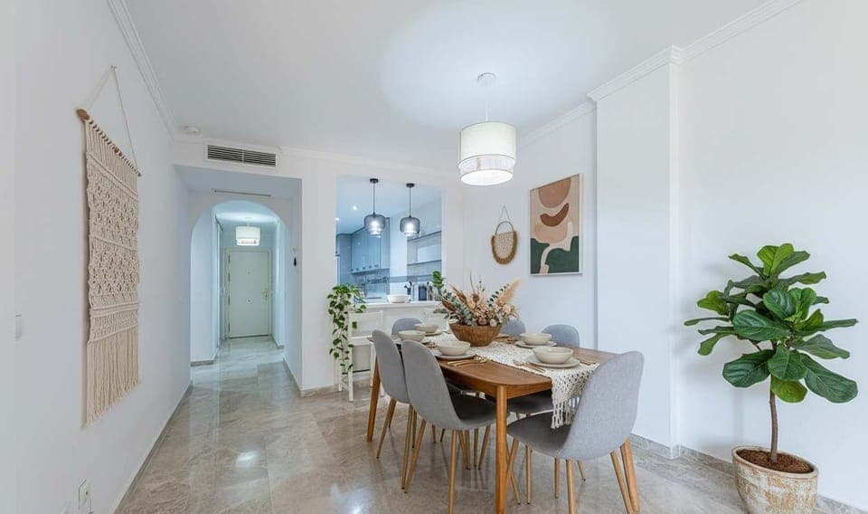 Dining area with a wooden table and gray chairs, leading to an open kitchen.