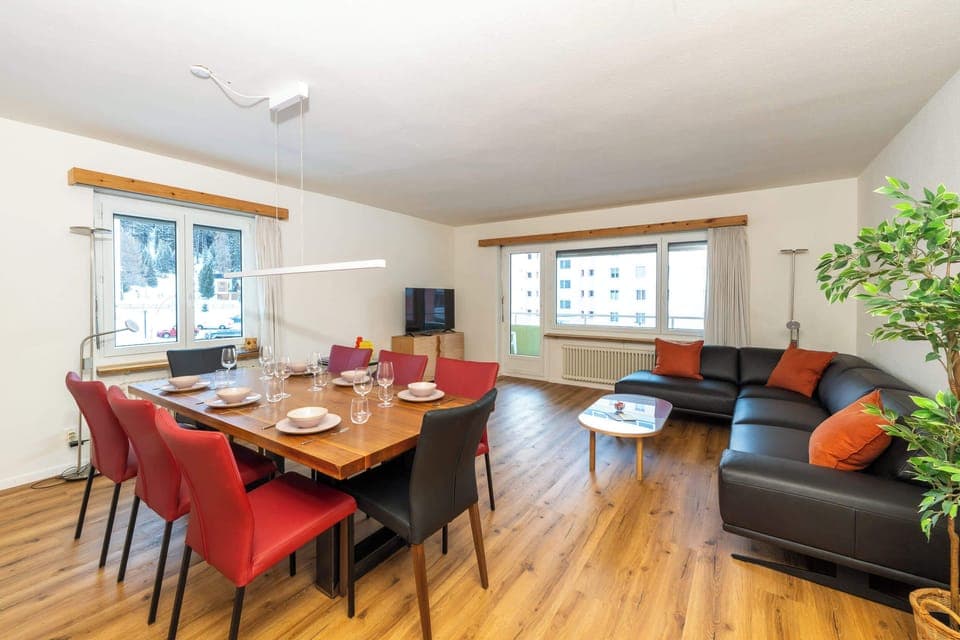 A spacious lounge with beautiful wooden floors, a long black sofa, and a wood-based dining table.