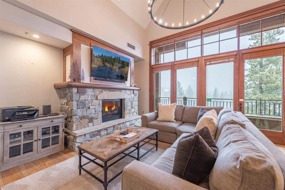 Sink into plush sofas beside your crackling fireplace while mountain vistas unfold through floor-to-ceiling windows. This cozy living room becomes your perfect retreat for evening relaxation.