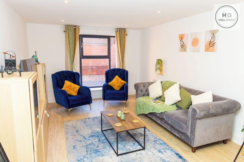 A spacious, beautifully designed living room with a cosy sofa, two velvet armchairs and warm lighting. Large windows bring in natural light, and the room’s modern décor creates a calm, comfortable atmosphere that makes you feel instantly at home.