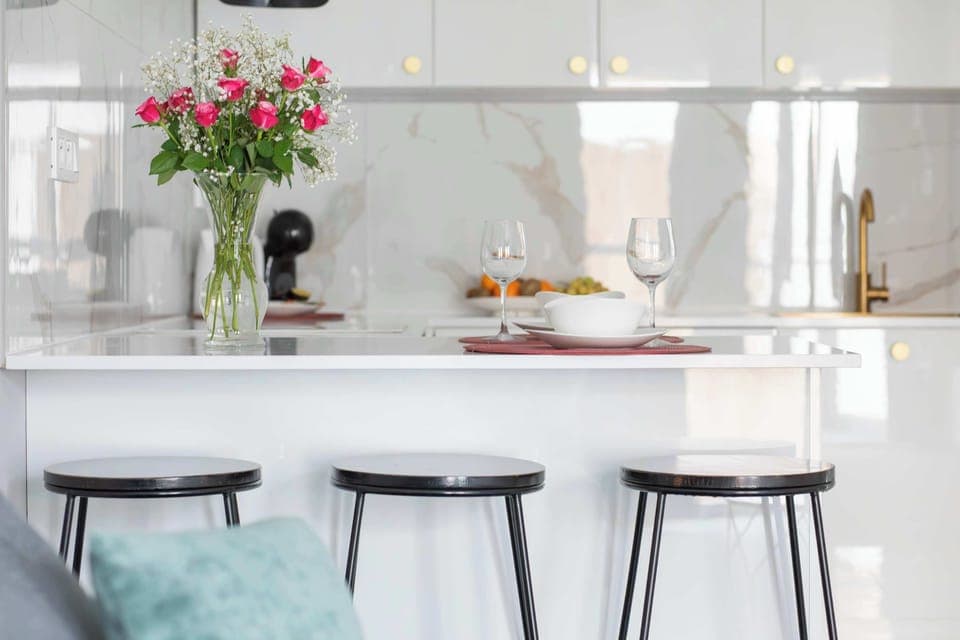 Another view of the white marble kitchen showcasing the countertop and elegant gold details. Decorative flowers add warmth to the modern design. The area looks pristine and stylish.
