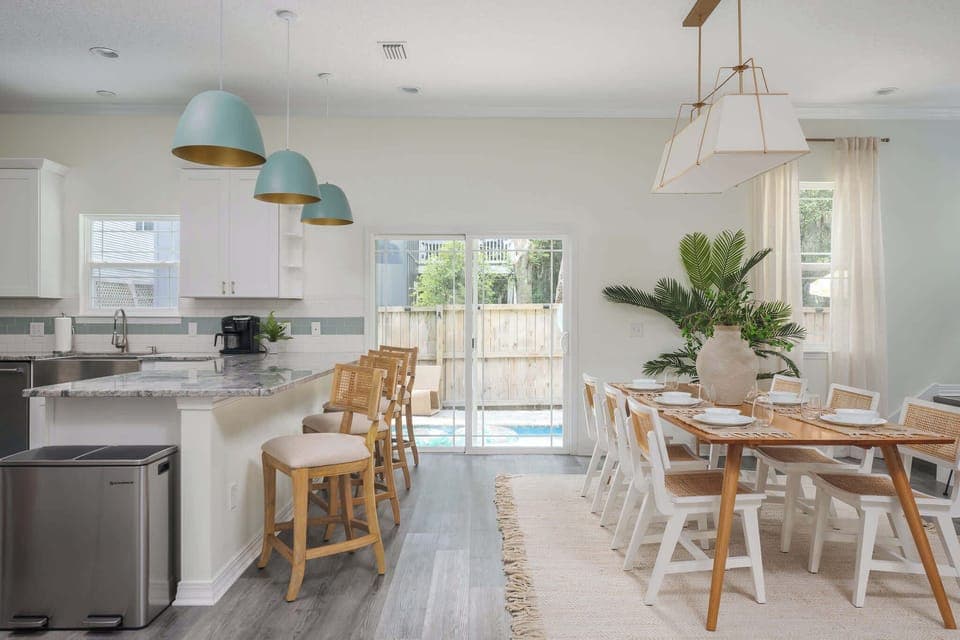 "Cook together in a bright, open kitchen with granite counters, sea‑glass lights, rattan stools and a farmhouse table. Slide open the doors and let the poolside breeze in for family dinners or happy hours. - The Coquina - St. Augustine, FL"