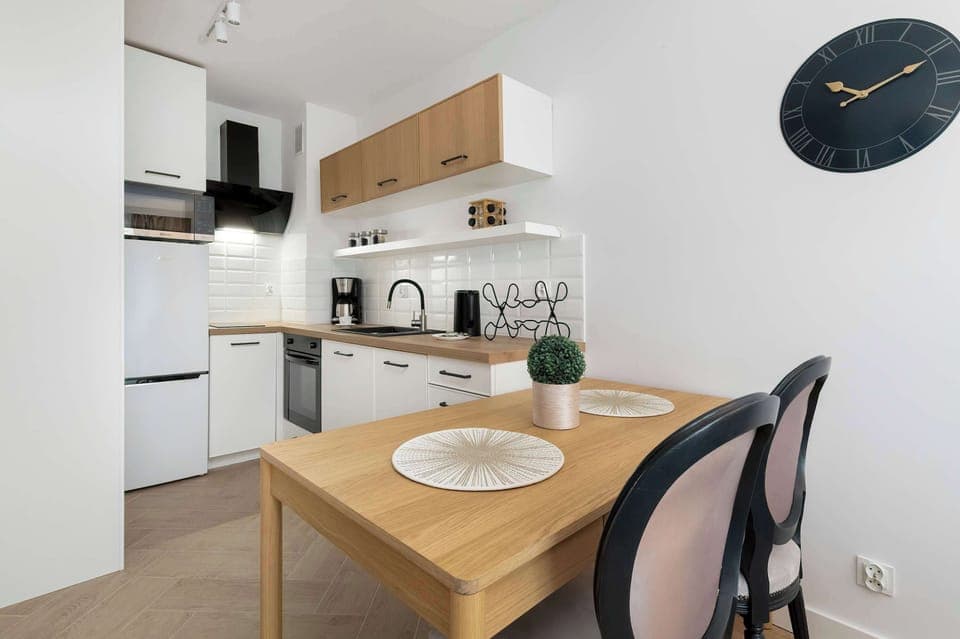 A compact kitchen with white cabinets, wooden countertops, and a small dining table with two chairs.