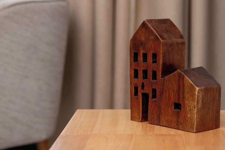 Decorative wooden house figurine displayed on a soft fabric surface.