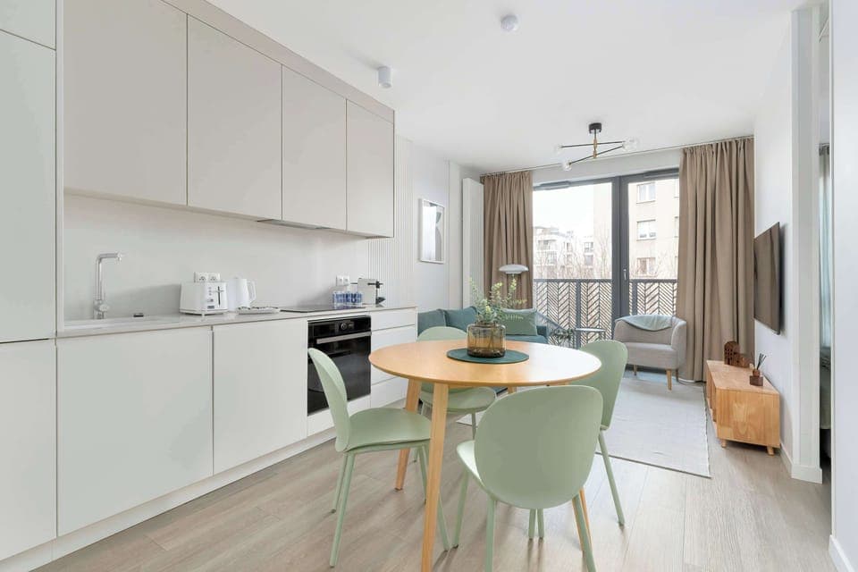 Modern kitchen with white cabinets, dining table, and large window.