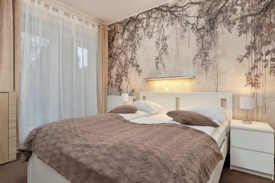 A cozy bedroom with a large bed and patterned wallpaper. Two bedside tables with lamps complete the inviting setup.