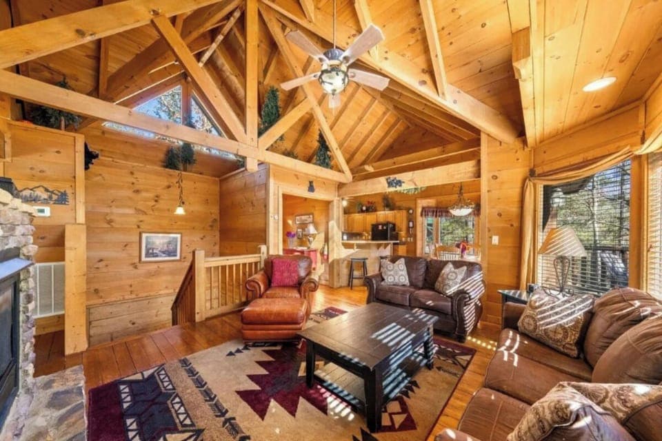 Relax in this stunning open-concept cabin living room with soaring wood-beamed ceilings and cozy leather seating around the warm fireplace.