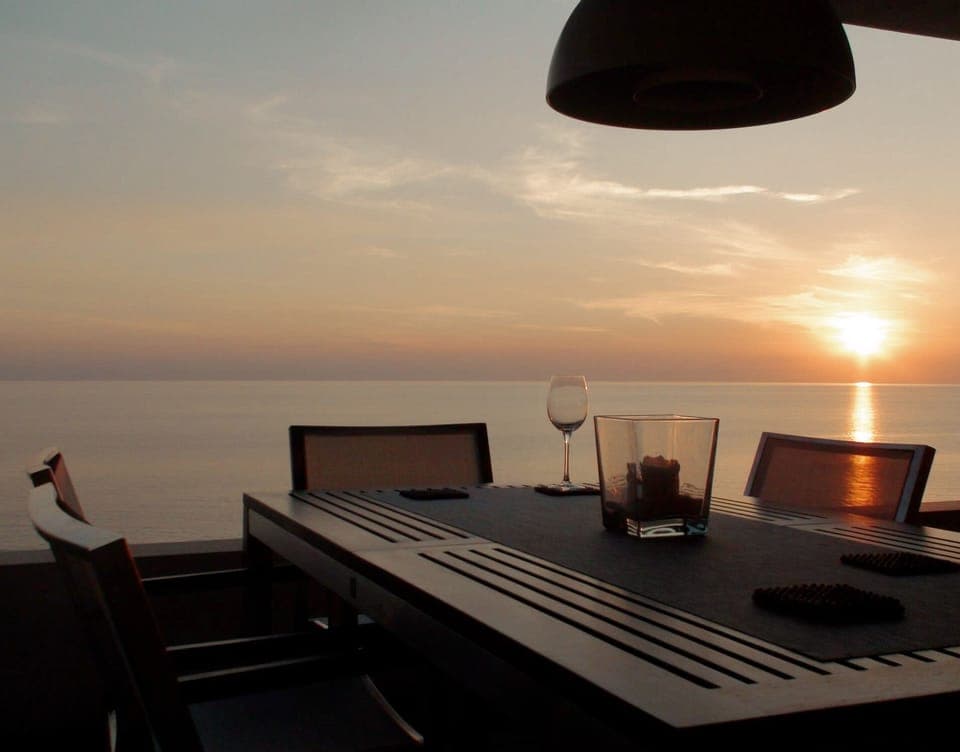 Outdoor dining table facing the sea at sunset, with open horizon views