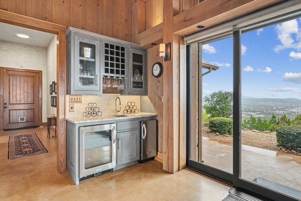 A charming wet bar nook featuring custom cabinetry, a built-in wine rack, and a mini fridge-perfect for entertaining or enjoying a quiet drink, this cozy space offers easy access to the outdoors and stunning hill country views.