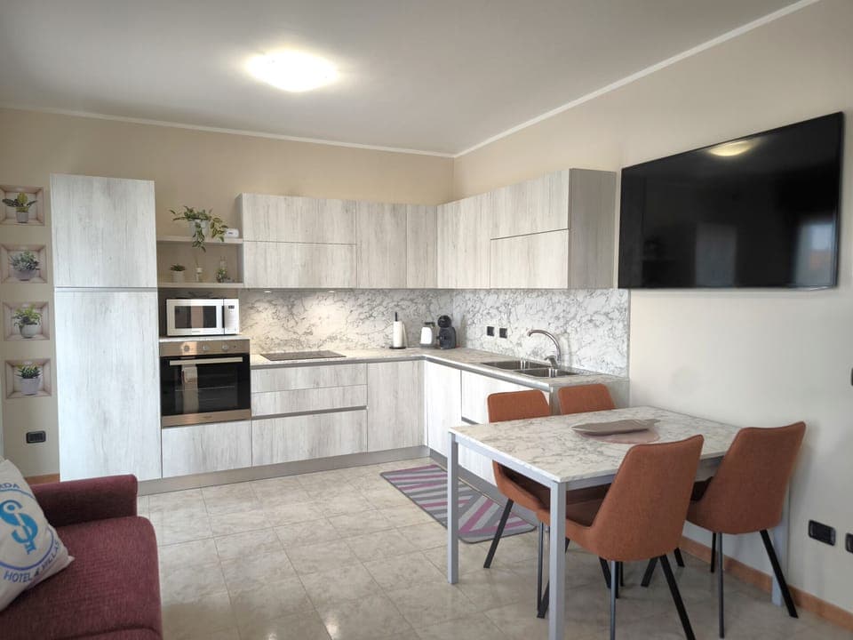 Fully equipped kitchen in the apartment in Peschiera del Garda, modern and functional, equipped with oven, microwave, and coffee machine. The bright room includes a comfortable dining area and a large TV, ideal for relaxing with family or friends.