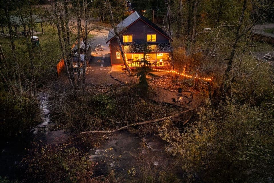 Drone twilight view of cabin, backyard, creeks, firepit and rope lighting