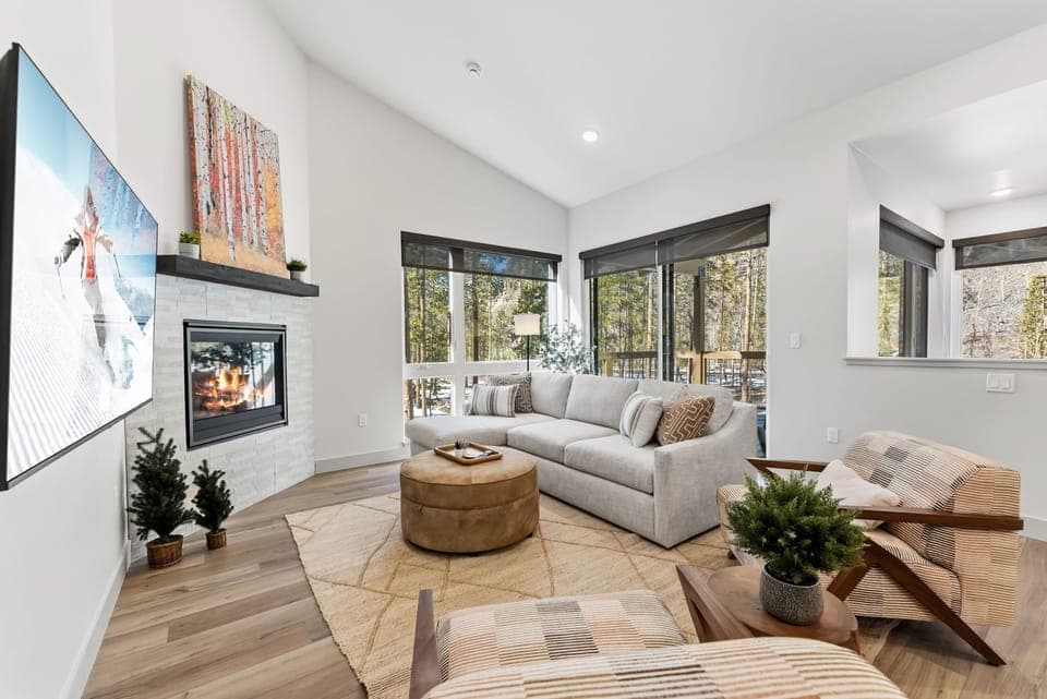Unwind in your bright living space with cozy fireplace, plush seating, and forest views streaming through panoramic windows.