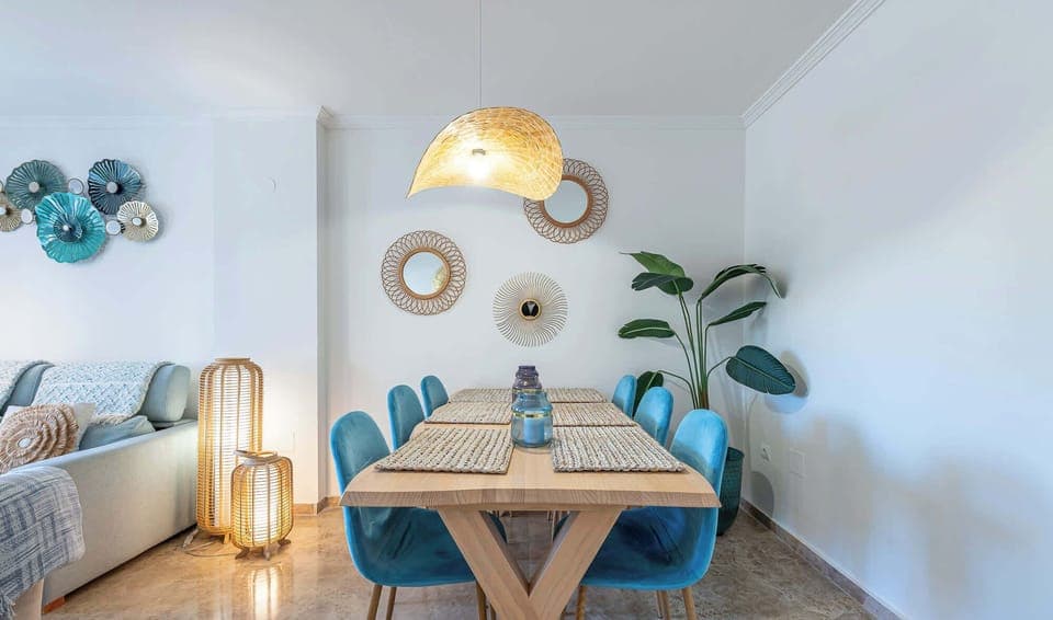 Stylish dining area with wooden table, blue chairs, and woven pendant light. Natural textures and warm tones create a welcoming, modern space.