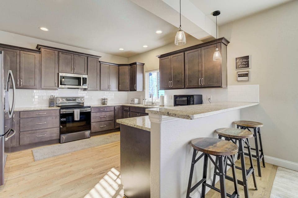 This fully stocked kitchen features professional-grade stainless steel appliances and dark wood cabinetry. The layout includes a modern gas range and a convenient breakfast bar with stool seating, providing a polished and functional space 