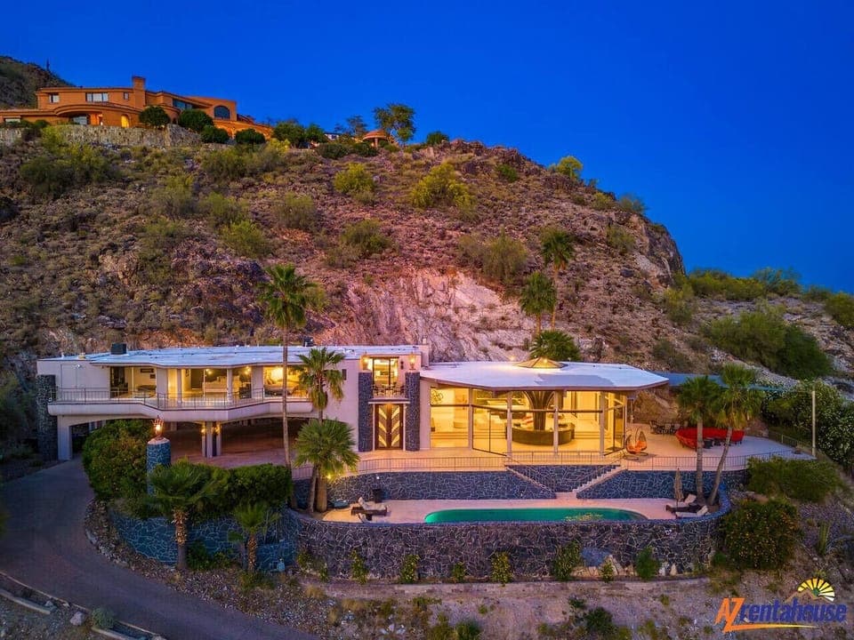 Modern hillside villa with stunning pool terrace illuminated against dramatic desert landscape at twilight.
