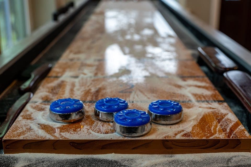 Close-up of a shuffleboard table showing blue pucks on the polished wooden playing surface with scoring zones.