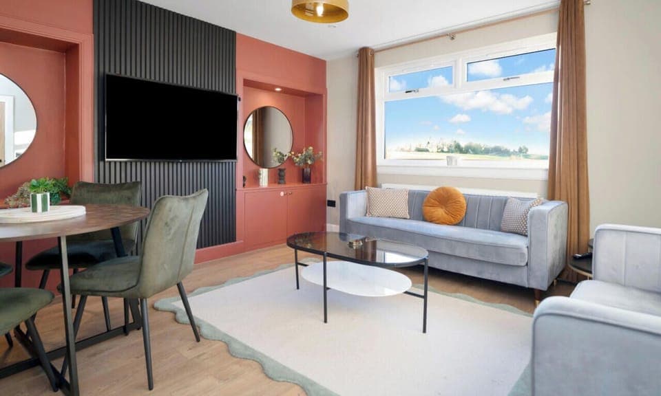 Living area furnished with a three-seater sofa, two-seater sofa, and smart TV.