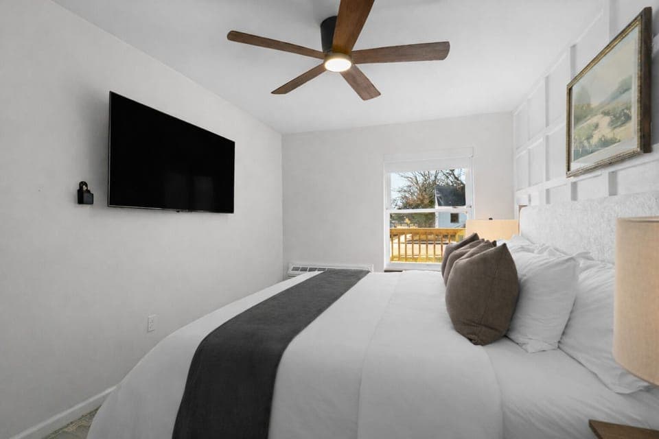 Peaceful bedroom with plush bedding, ceiling fan, and wall-mounted TV—designed for restful nights and a relaxing, comfortable stay.