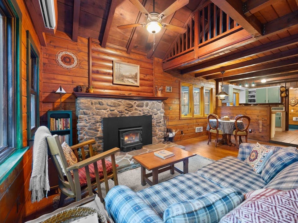Cozy up in this rustic log cabin retreat with stone fireplace, plaid furnishings, and warm wood beams creating your perfect mountain getaway.