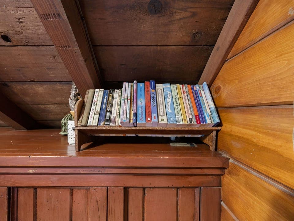 Curl up with your favorite book from this charming collection, perfectly arranged in your cozy wooden retreat.