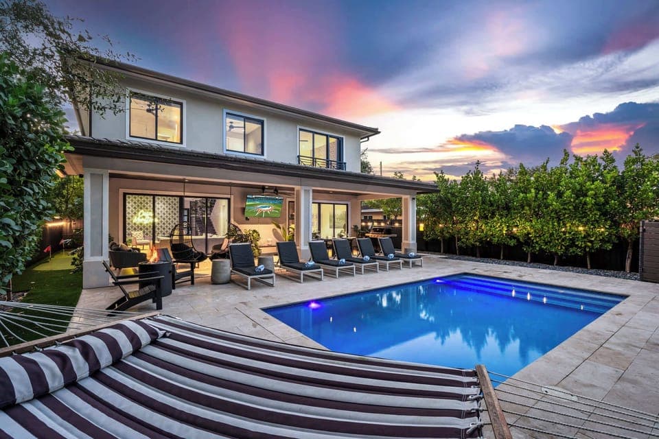 Outdoor patio with 75" Smart TV for streaming games or your favorite movie. Firepit, Adirondack chairs, golf putting green, hammock, string lights, BBQ grill, outdoor dining table for twelve, and heated salt water pool.